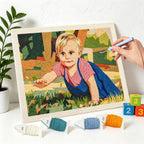 Framed needlepoint of a child in a garden with yarn and tools on a white surface.